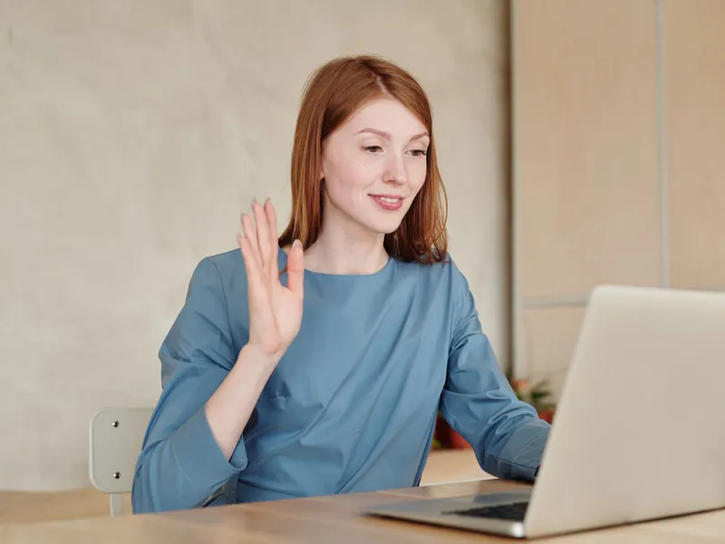 Mosolygó nő integet a laptopja kamerájának egy videohívás elején